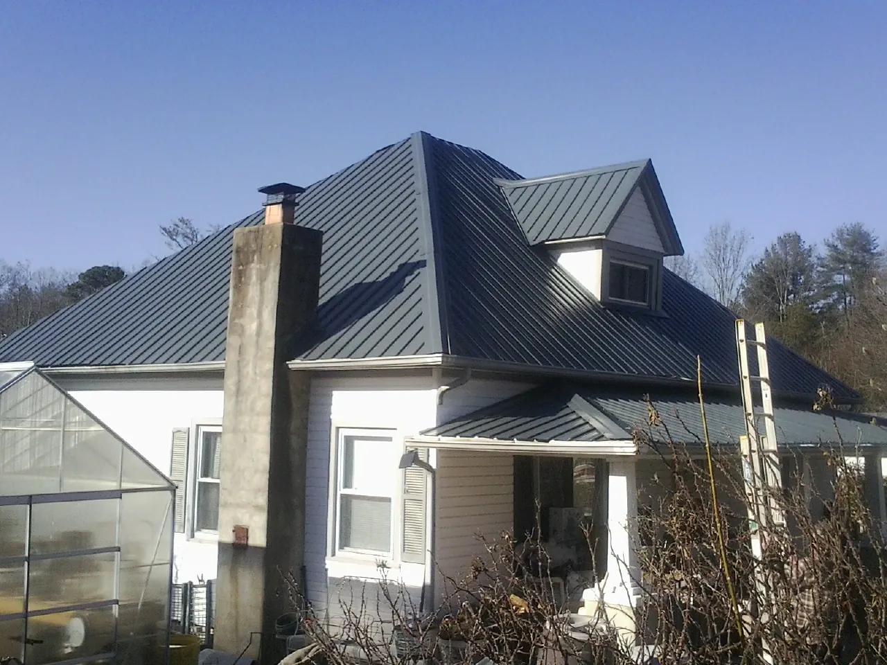Dark blue standing seam metal roof on a white farmhouse with dormer — Slate & Tile Roof Repair by Roofing Brothers in Donaldsonville