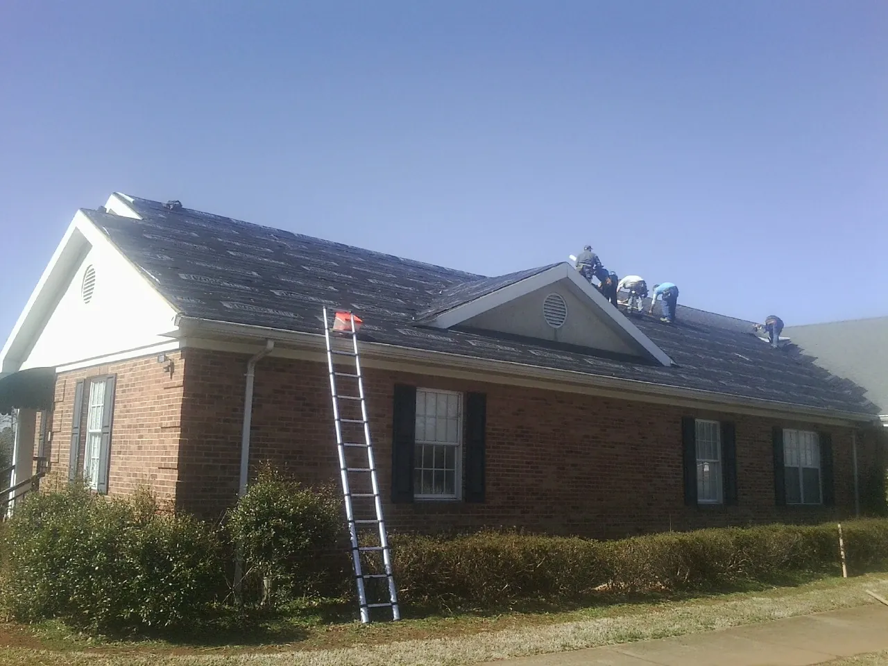 Crew tearing shingles off a brick ranch roof with a ladder set — Emergency Roof Repair work by our crew in Donaldsonville