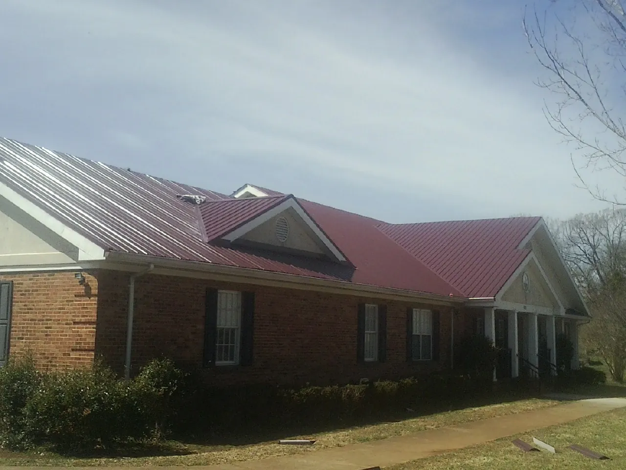 Red metal roof with gabled entries on a long brick building, from a Hail Damage Roof Repair job in Donaldsonville
