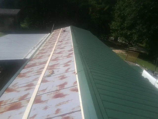 Old rusted panels beside newly installed green metal roofing — Wind Damage Roof Repair by Roofing Brothers in Donaldsonville