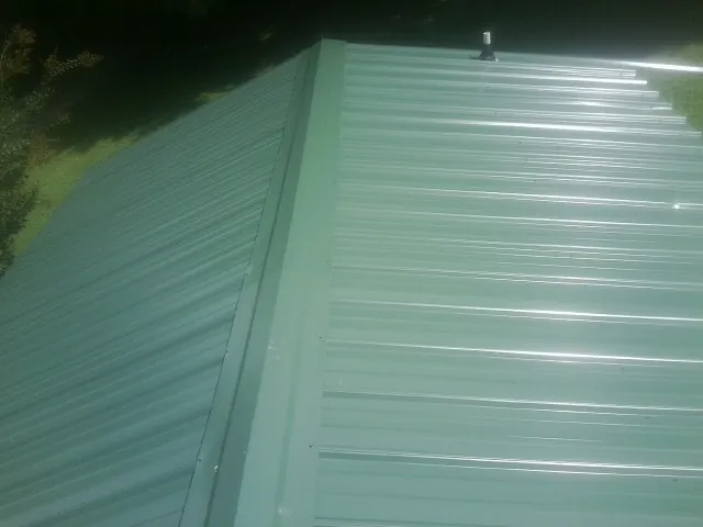 New green metal panels meeting at the ridge of a roof — Flat Roof Repair work by our crew in Donaldsonville