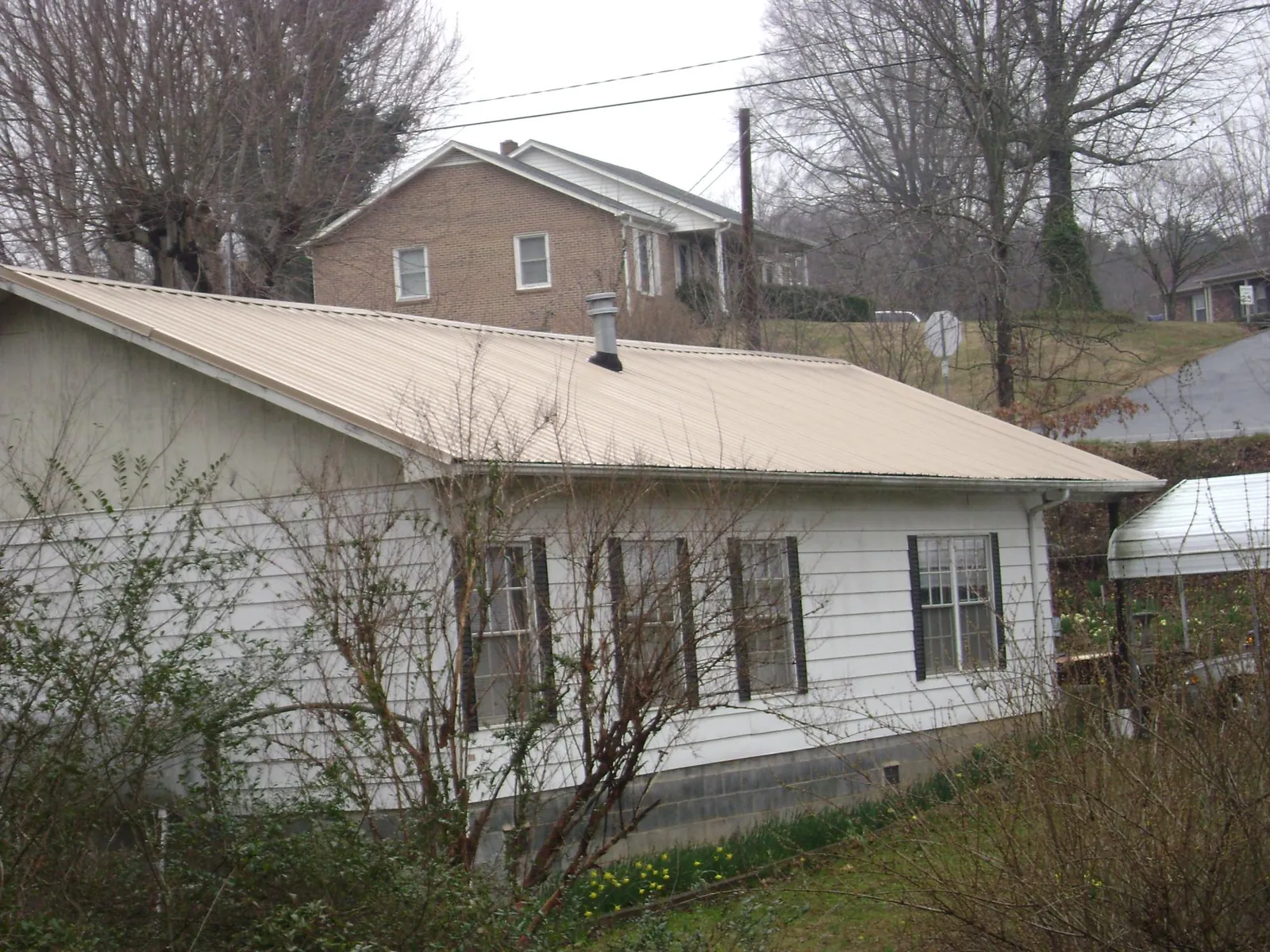 Tan metal roof on a white sided house set into a hillside — Commercial Roofing by Roofing Brothers in Donaldsonville